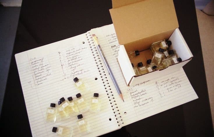Small glass vials of perfume in an open box beside handwritten notes
